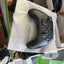 A matte black Xbox One S wireless controller resting on a crumpled piece of white paper inside an open box, surrounded by packaging materials and cables.