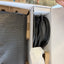An open cardboard box showing a black textured rectangular item wrapped in protective material and a coiled black power cable inside a white box.