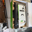 An open Xbox product box showing the contents, including a black textured accessory, a white instruction booklet with Xbox controller graphics, and cardboard inserts, photographed in a cluttered indoor setting.
