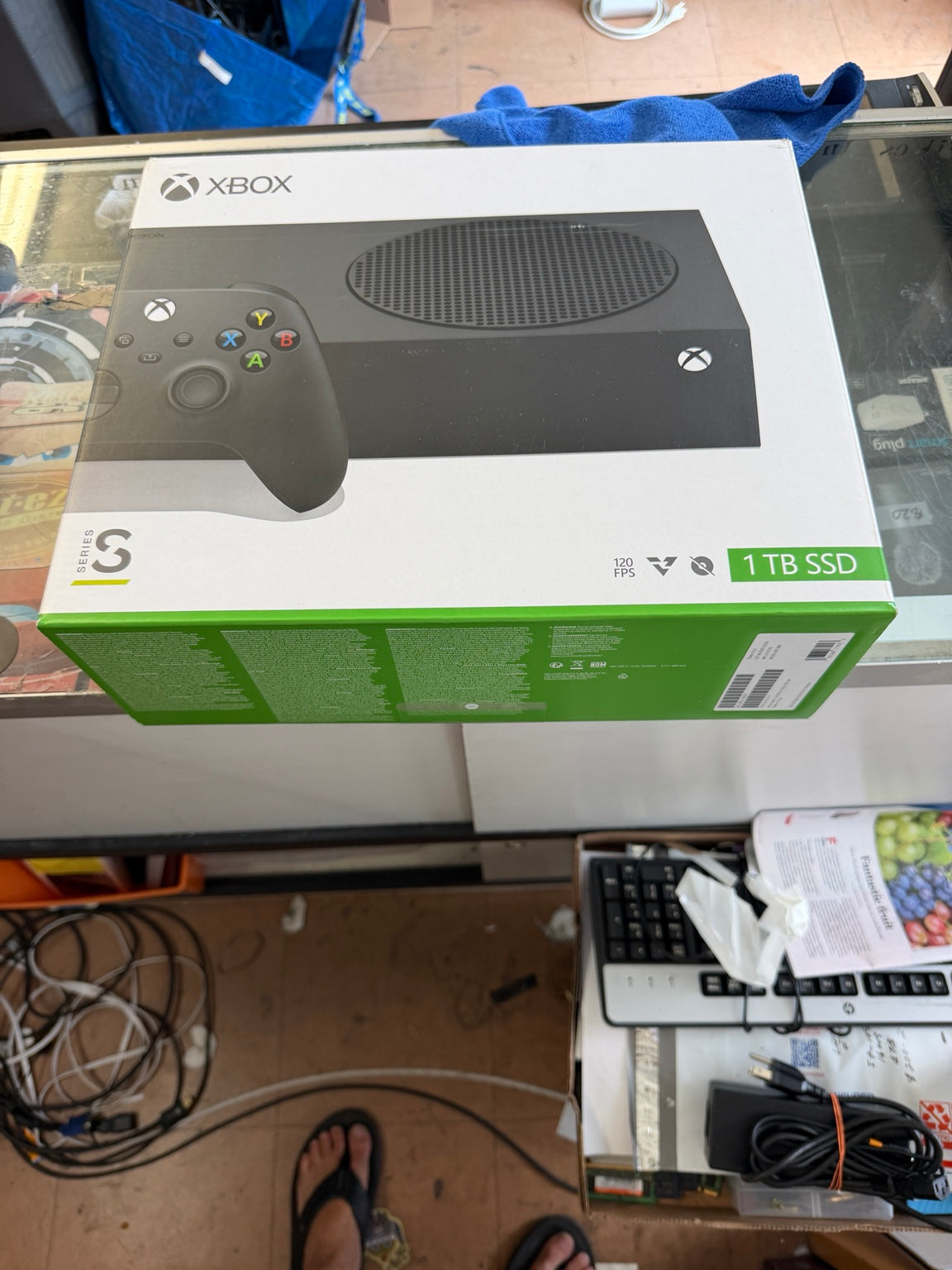 Xbox Series S 1TB SSD console retail box on a glass display counter in a retail store, with a controller pictured on the front of the packaging.