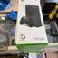 Xbox Series S 1 TB SSD retail box shown on a glass display counter in a store. The white box features a photo of the black console and controller, with green accents at the bottom.