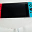 Nintendo Switch console with a black screen and bright blue and red Joy-Con controllers attached, resting on a white surface.