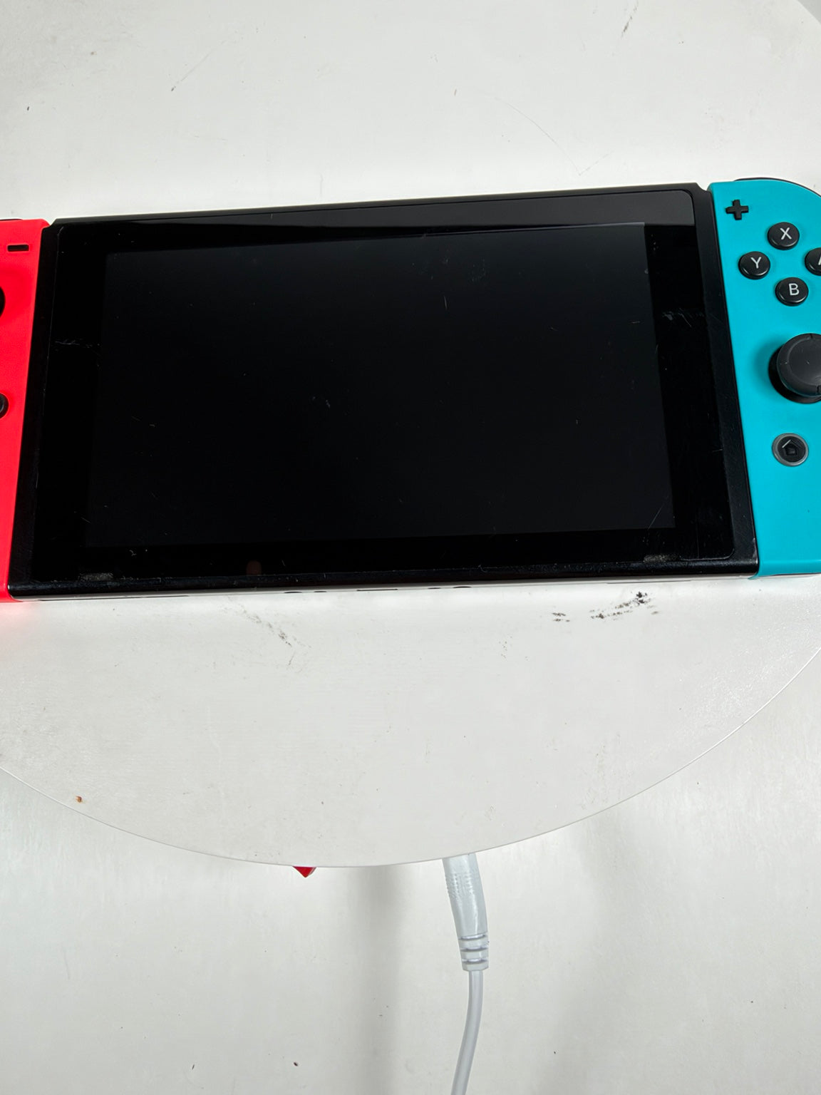 Nintendo Switch console with a black screen and bright blue and red Joy-Con controllers attached, resting on a white surface.
