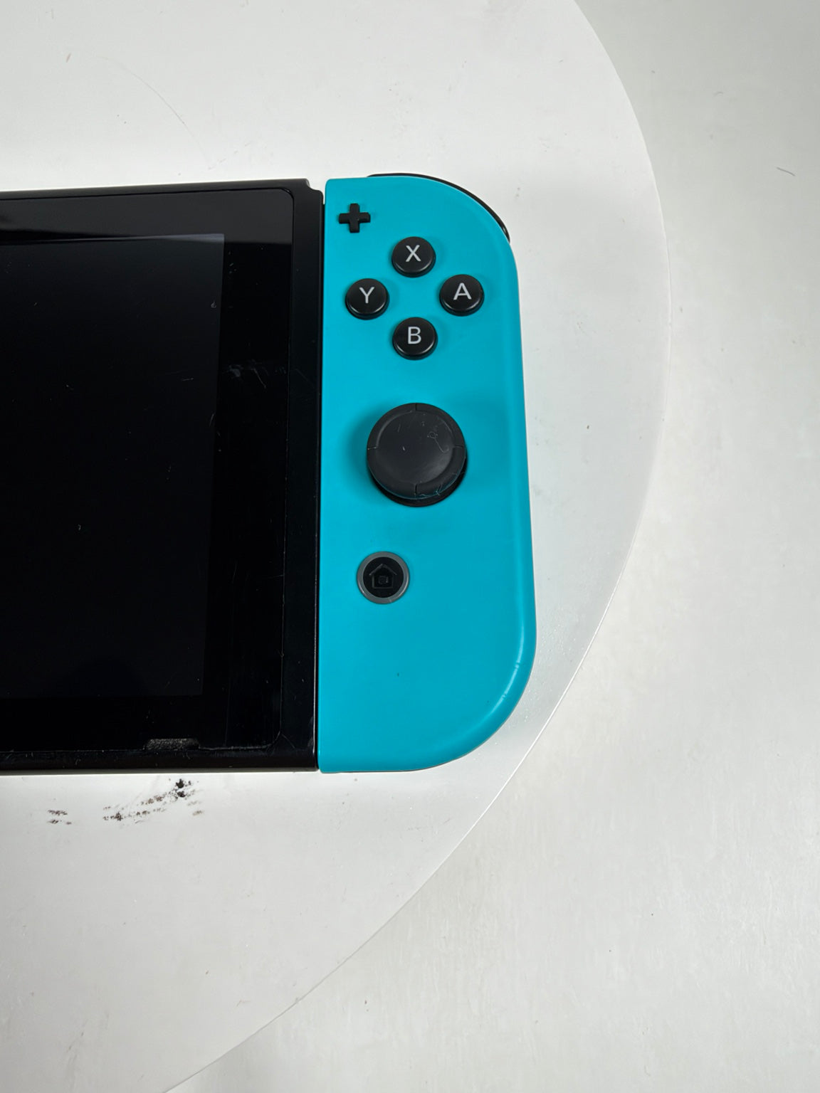A close-up of a Nintendo Switch console with a bright turquoise blue Joy-Con controller attached, resting on a white surface.