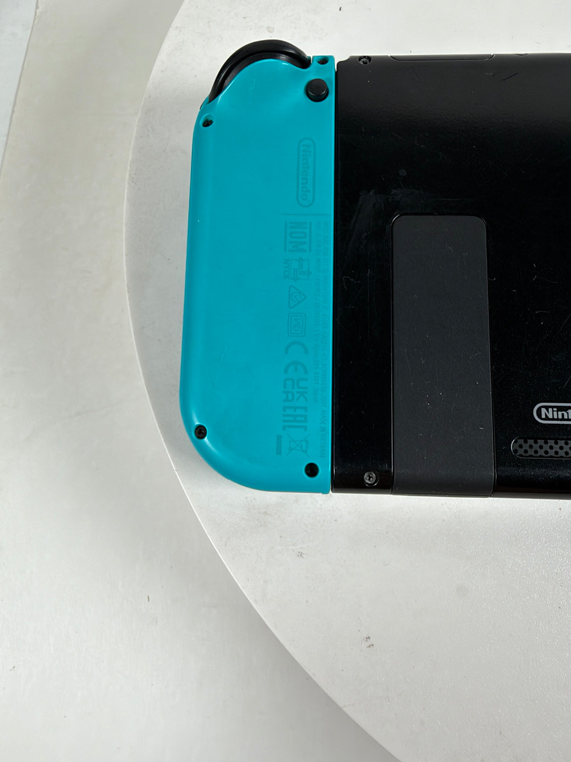 Nintendo Switch console with a bright turquoise blue Joy-Con grip attached to a black body, photographed on a white curved surface.