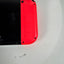 Nintendo Switch Lite console showing the underside with a bright red Joy-Con grip attached to a black body, photographed on a white surface.