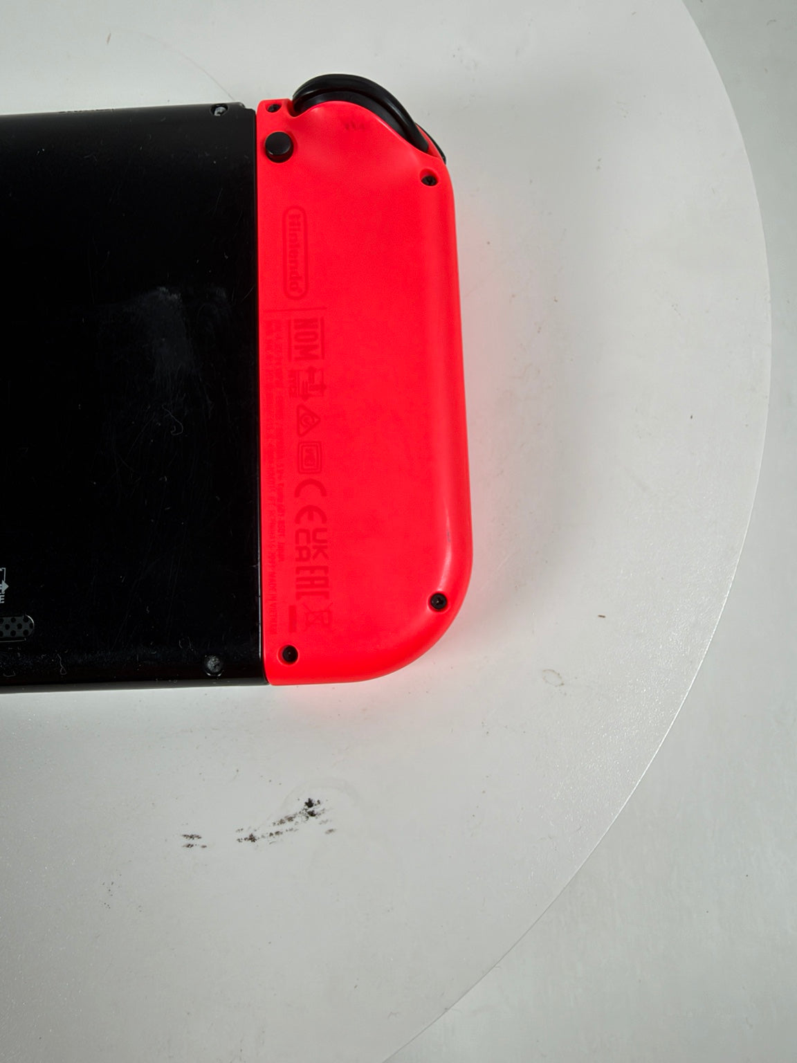 Nintendo Switch Lite console showing the underside with a bright red Joy-Con grip attached to a black body, photographed on a white surface.