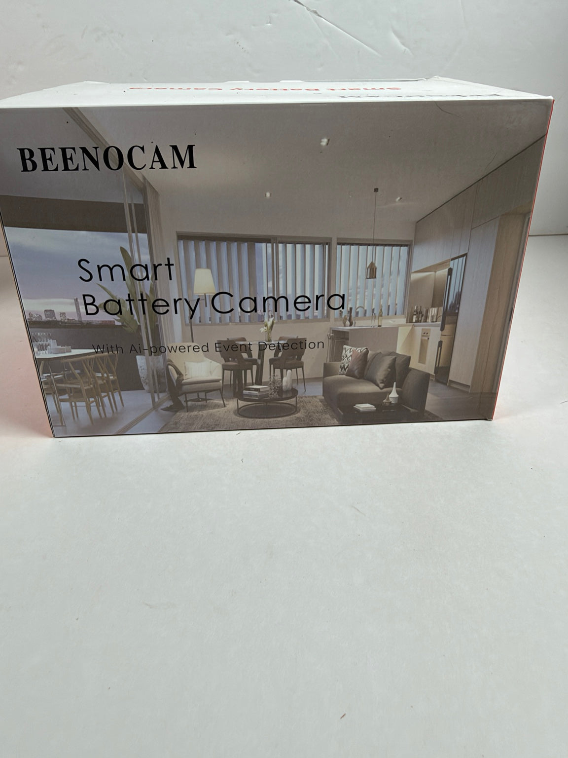 A boxed smart battery camera product labeled BEENOCAM, shown standing on a light surface. The front of the box features a grayscale interior room photo and the text 'Smart Battery Camera' and 'with AI-powered smart detection.