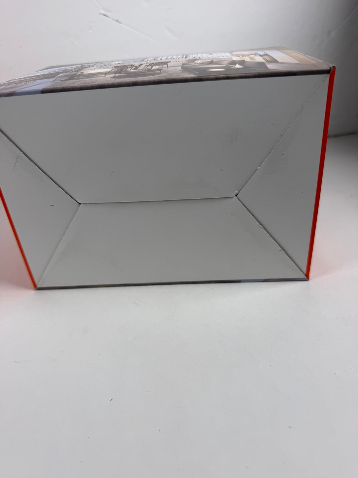 A cardboard product box photographed on a plain light surface, showing the inside bottom panel and side edges with a thin red outline.