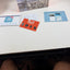 A person's legs are visible at the bottom of the frame, looking down at a white desk surface containing a Beenocam Smart Battery Camera box, a blue instruction booklet, a red TEMU card, and a white card with a blue logo.