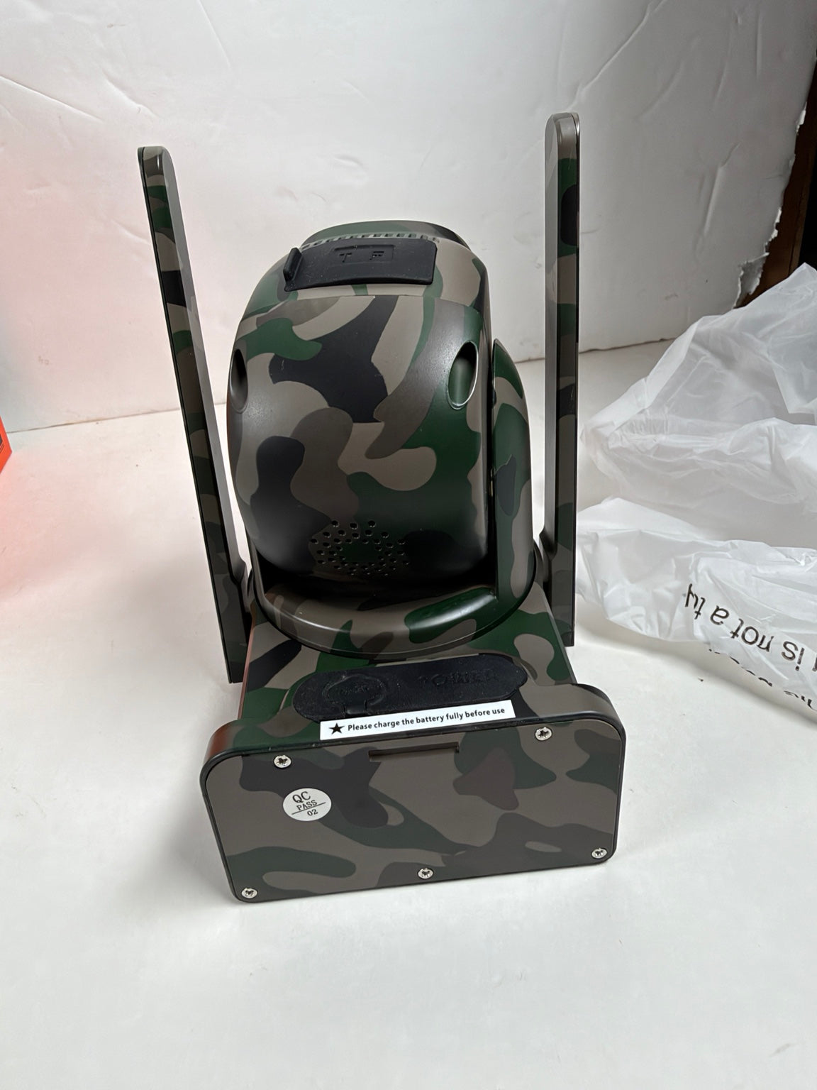 A camouflage-patterned electronic device with two vertical antennas, standing on a matching camouflage base against a white background.