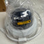 A white dome security camera still in its clear plastic packaging, showing the protective film and a yellow warning label on the front.