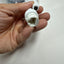 A hand holding a white plastic RJ45 connector with a short cable attached, with a plastic-wrapped item in the background on a light surface.