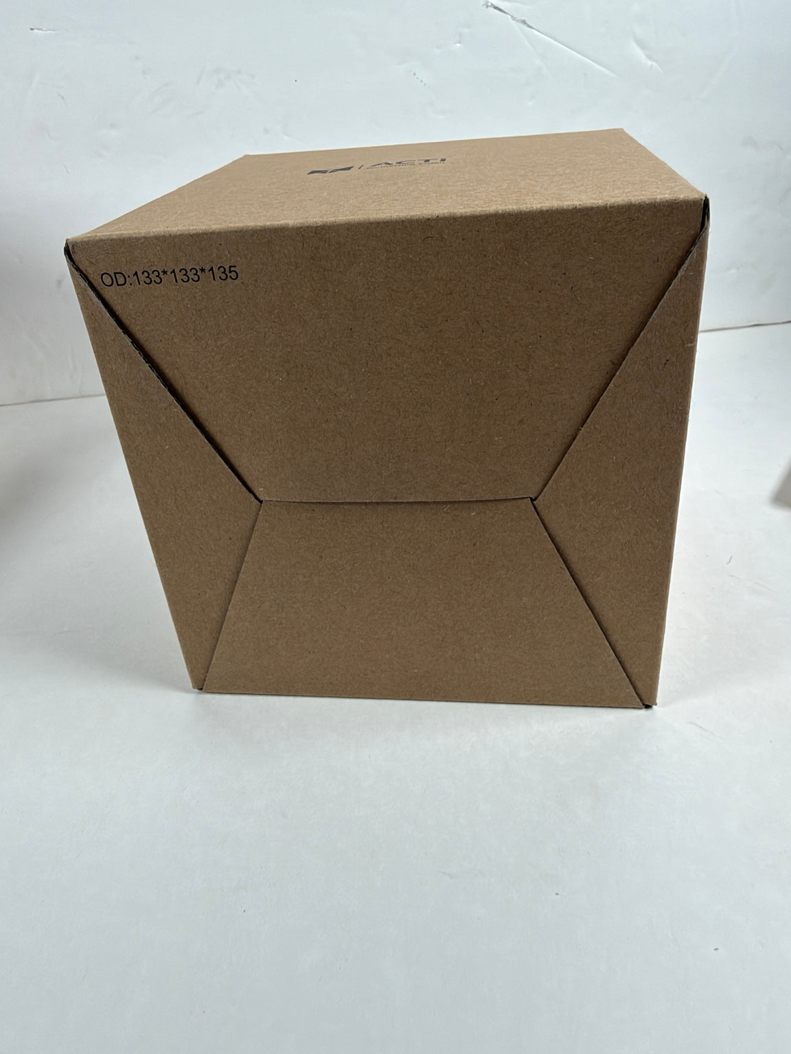 A plain brown cardboard box photographed on a white surface against a white wall. No person, animal, or real environment beyond the simple studio-like setup is present, so this is Product/Packaging.