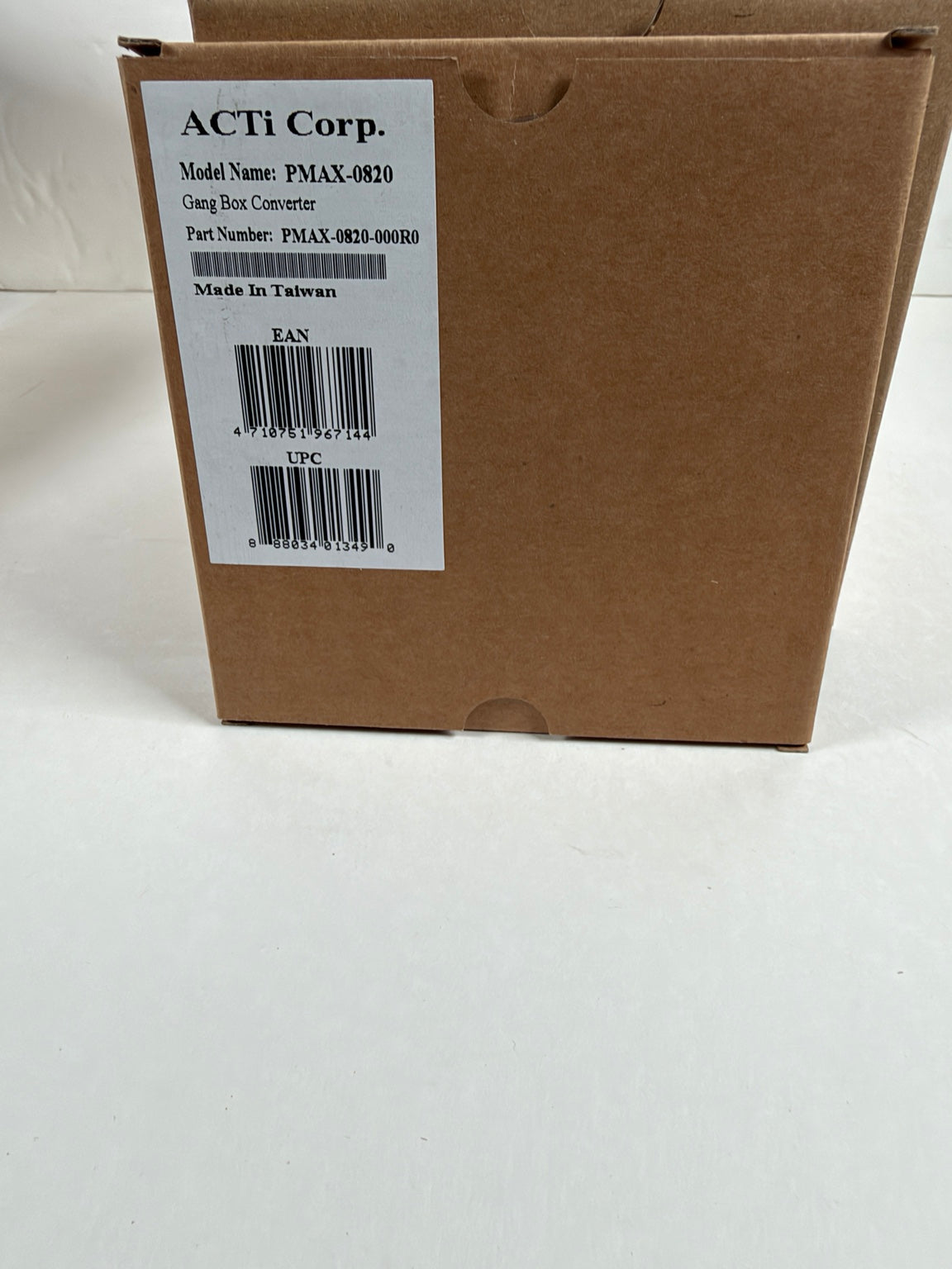 A brown cardboard shipping box with a white label from ACTi Corp. showing product details, photographed on a white surface.