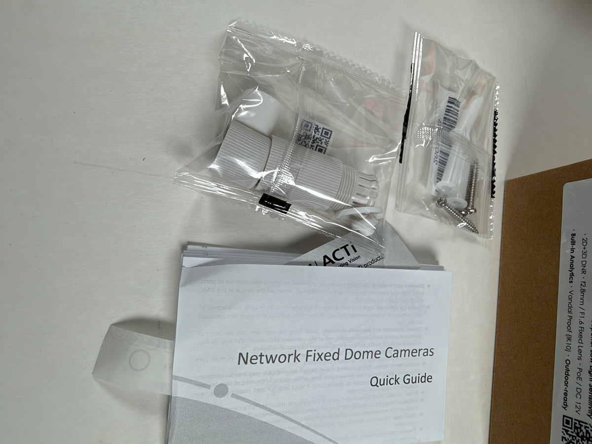 A Network Fixed Dome Cameras Quick Guide booklet with its clear plastic packaging accessories, including a white mounting bracket and screws, laid out on a light surface.
