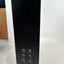 A tall black product box standing upright on a white surface against a white wall, with small white feature icons printed near the bottom.
