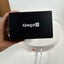 A hand holds a black Abegal S product box in front of a white circular device on a white surface against a white wall.