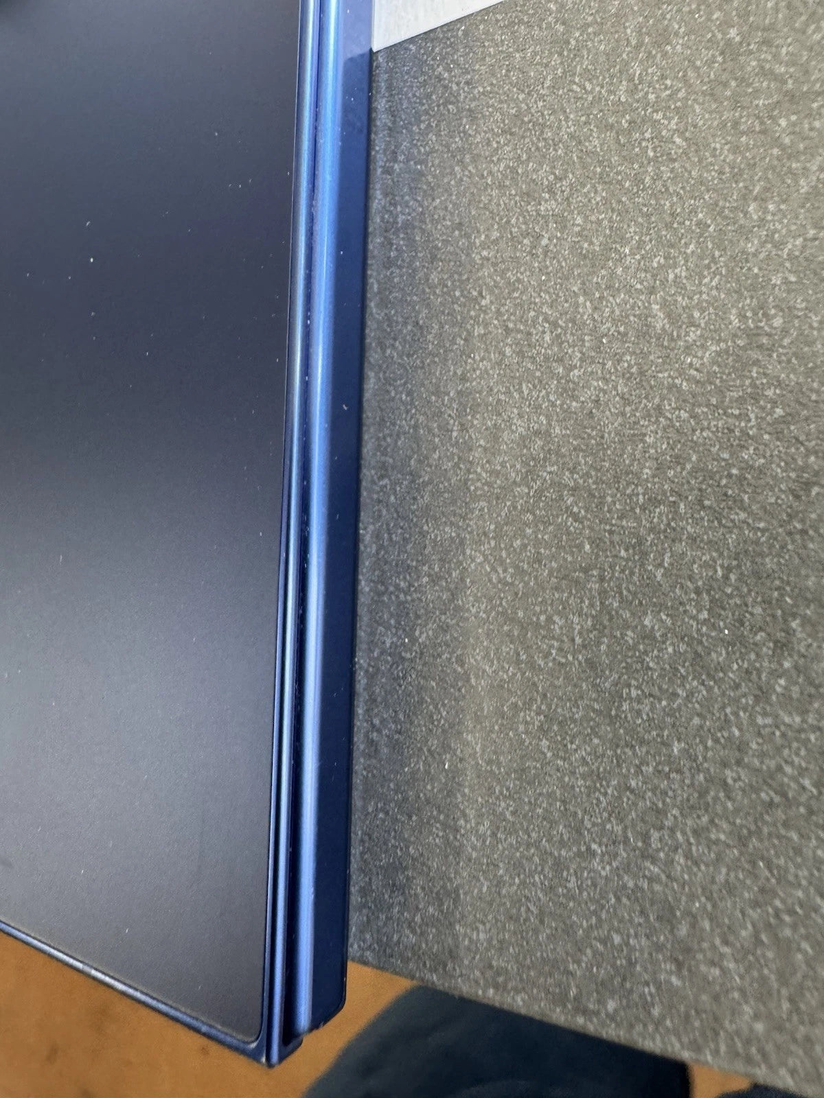 Close-up of a dark blue or black rectangular object with a thin metallic blue edge, positioned next to a textured gray surface.