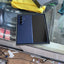 A Samsung Galaxy S24 Ultra smartphone in a dark blue and black finish, shown inside its original retail box on a glass desk with a yellow microfiber cloth and accessories.