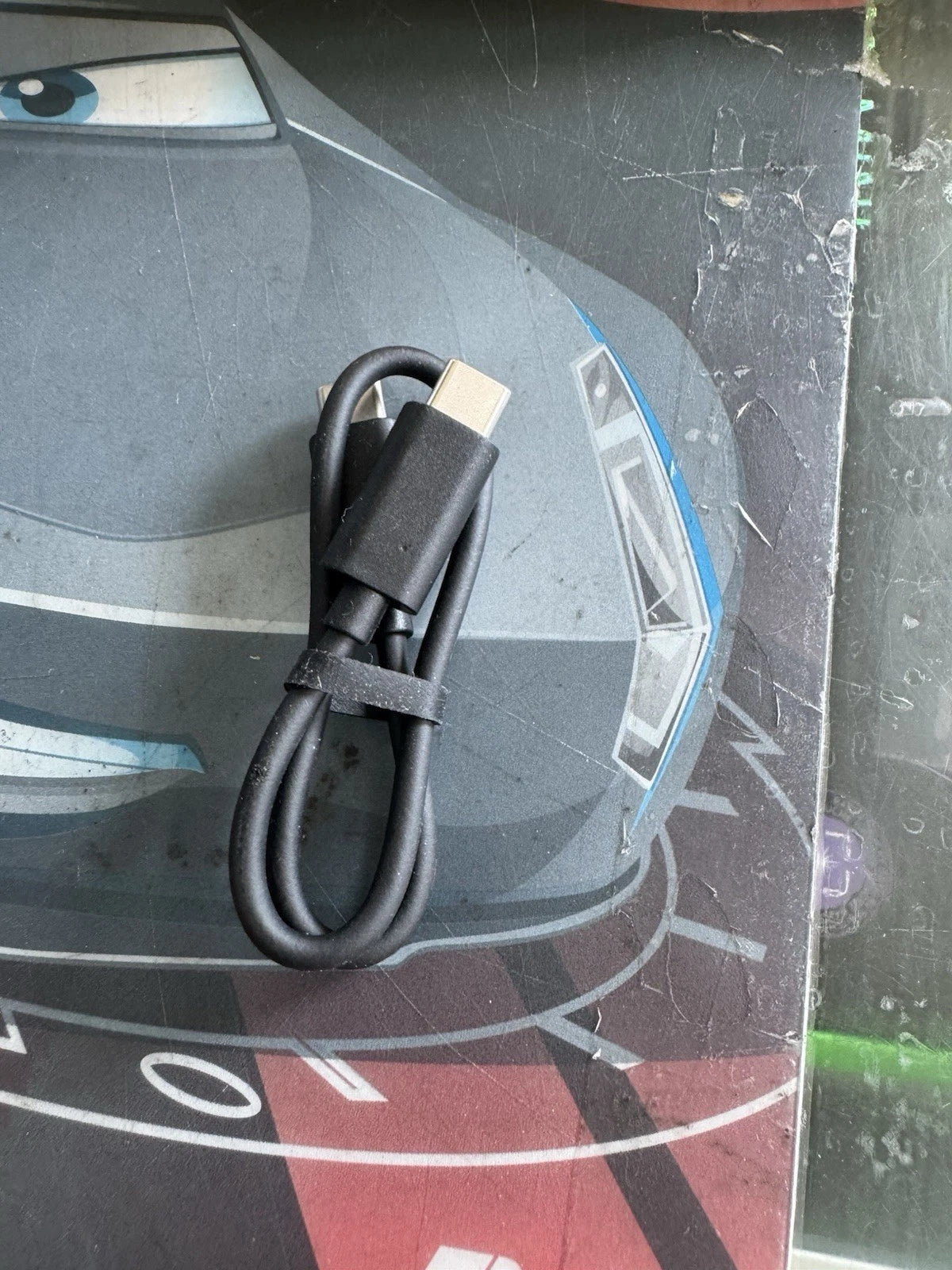 A black USB-C to USB-A data and charging cable coiled with a black elastic band, resting on a dark printed surface.