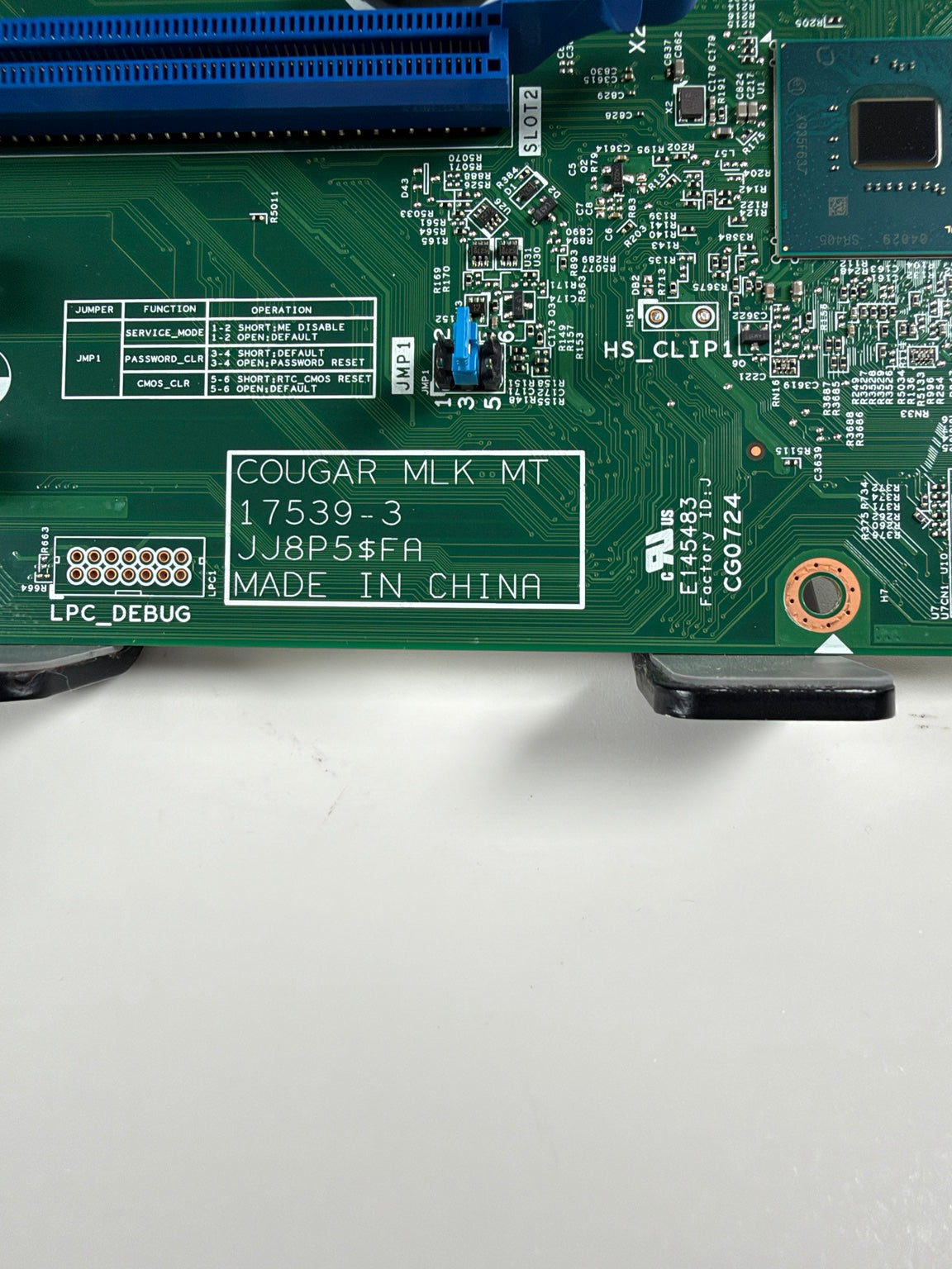 Close-up of a green motherboard circuit board showing printed labels, a blue PCIe slot, and a white sticker with the text 'COUGAR-MLK MT 17539-3 J8P5$FA MADE IN CHINA'.