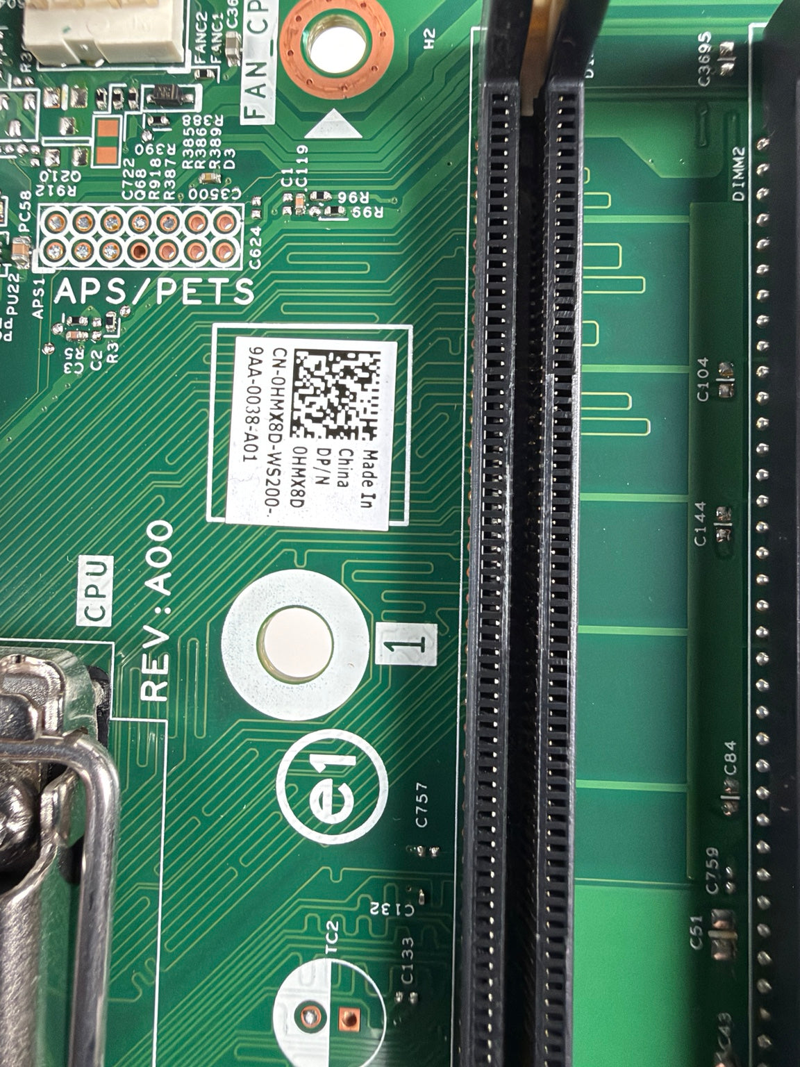 Close-up of a green printed circuit board showing a black PCIe slot, connector pins, white labeling stickers, and technical component markings.