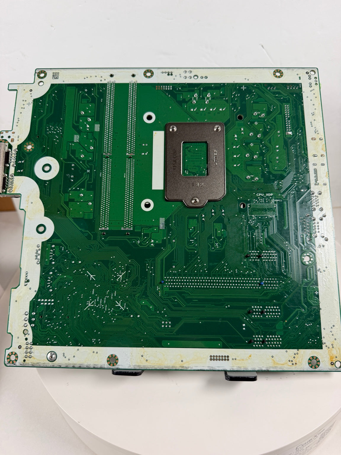 A green printed circuit board assembly with a central metal mounting bracket, photographed from above on a white surface.