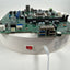 A green computer motherboard with integrated USB ports, shown resting on a white circular charging or display base with a power switch and cable attached. The brand name Core-Kim is visible on the base.