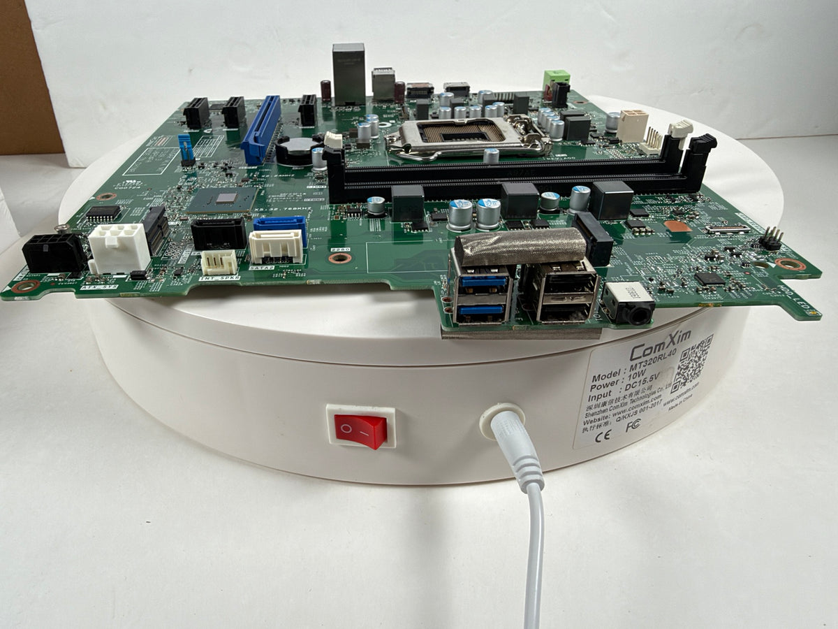 A green computer motherboard with integrated USB ports, shown resting on a white circular charging or display base with a power switch and cable attached. The brand name Core-Kim is visible on the base.