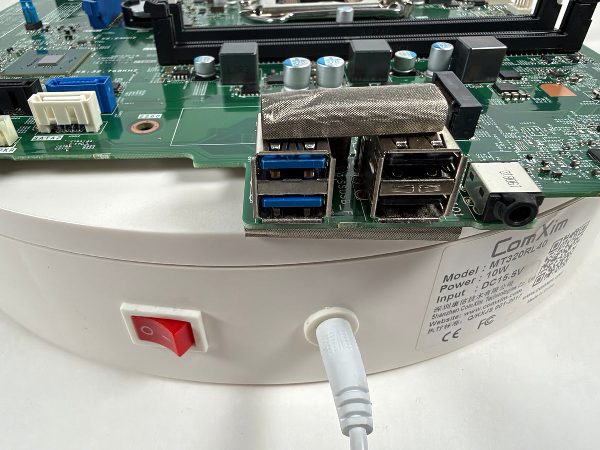 Close-up of a white cylindrical electronic device with a red power switch and a power cord plugged into it, showing a green circuit board with USB ports and a metal mesh component.