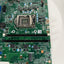 A green Dell motherboard with an LGA 1200 CPU socket, RAM slots, and various electronic components, photographed from a top-down angle on a white surface.