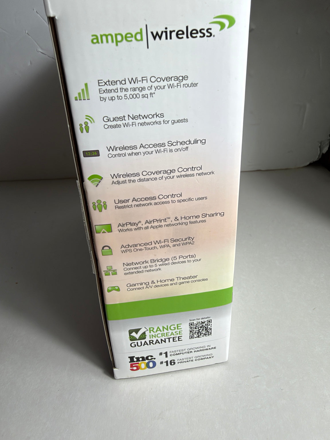 A tall white product box for Amped Wireless, showing feature callouts in black text with green and gray accents, photographed on a gray surface.