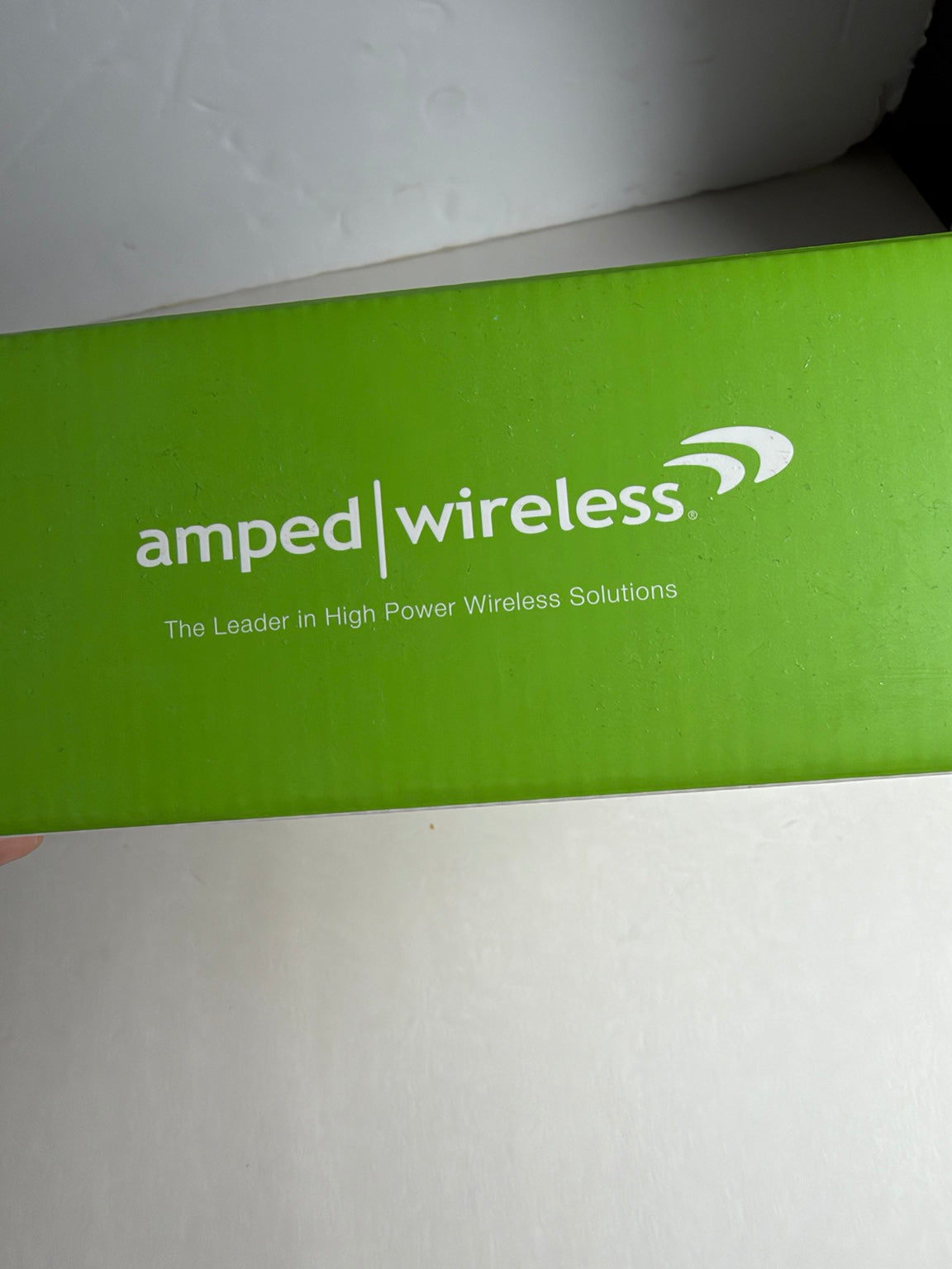A close-up of a bright green Amped Wireless product box with white printed branding and the tagline 'The Leader in High Power Wireless Solutions' on a light surface.