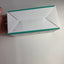 A white rectangular product box with teal-green edges, held by a hand on a plain white surface.