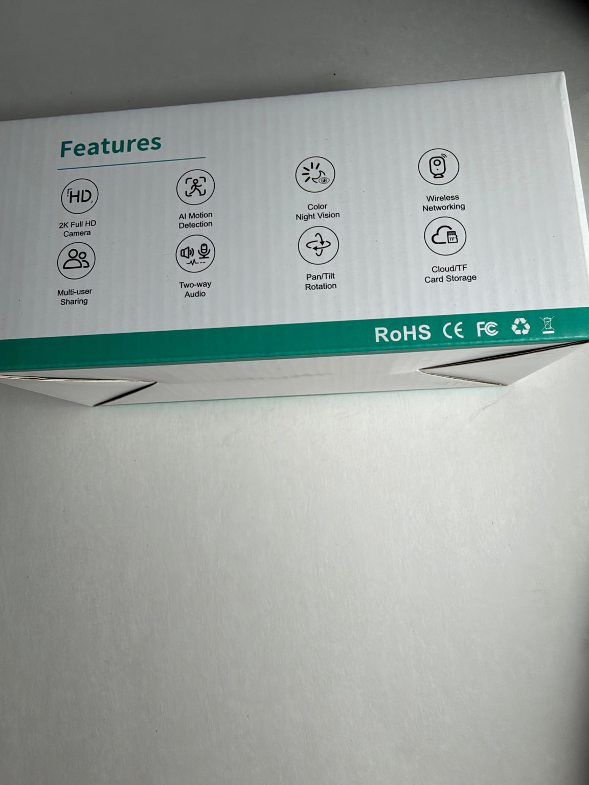 A white product box with a teal band at the bottom, featuring printed feature icons and text such as HD, AI Motion Detection, Color Night Vision, and CloudTF Card Storage.