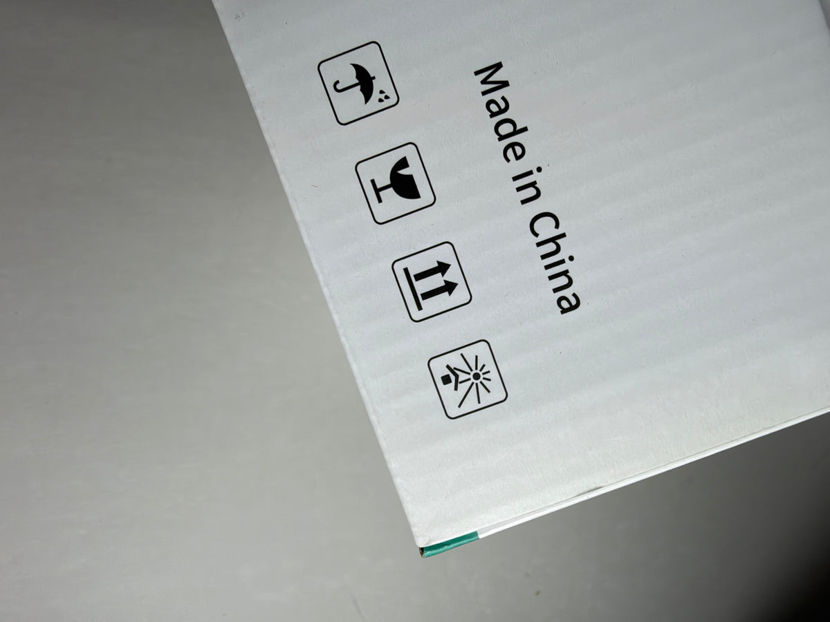 A close-up of a white corrugated cardboard box corner with printed black handling icons and the text 'Made in China' on a gray surface.