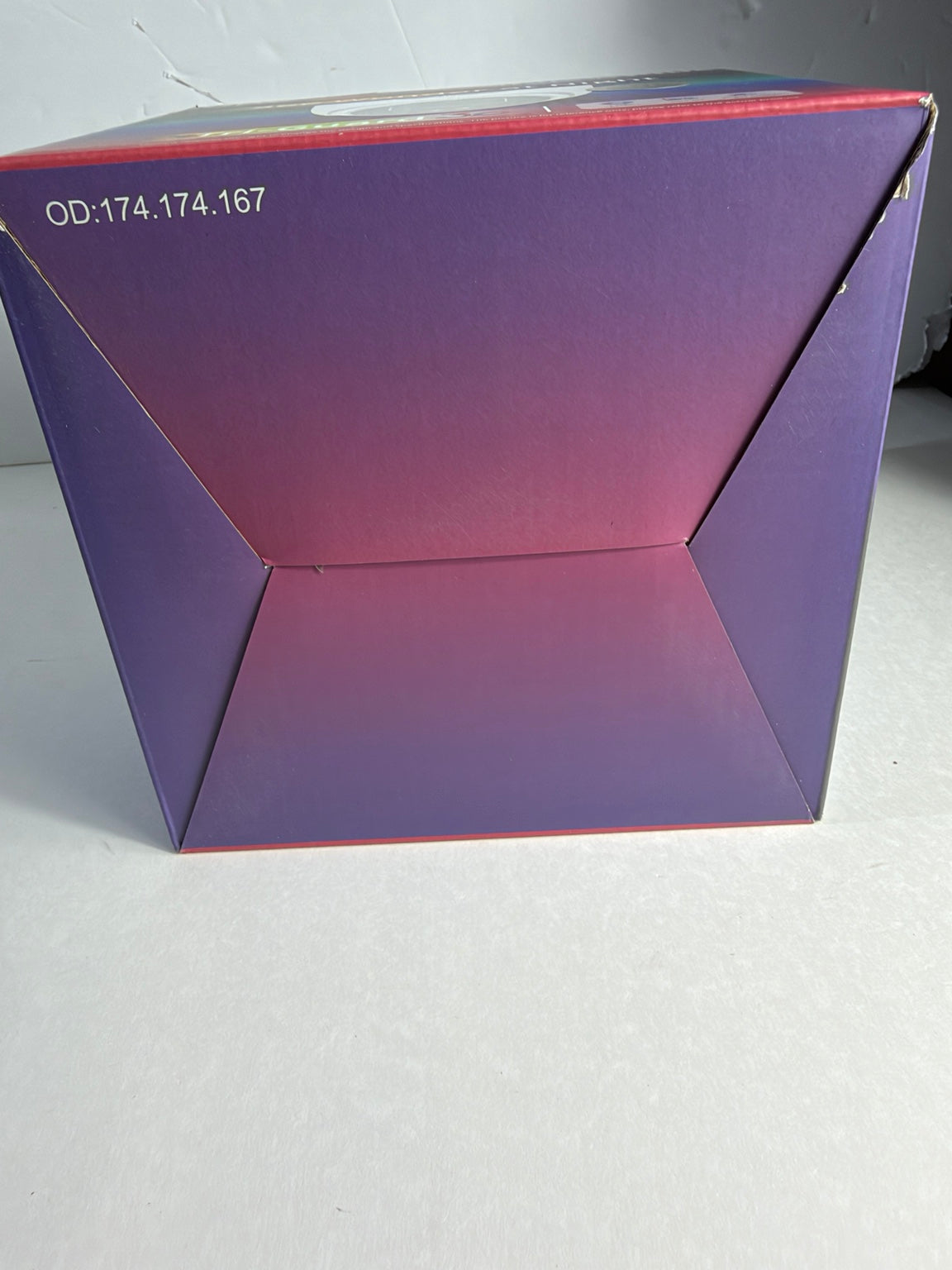 A square product box with a purple and pink gradient design, photographed on a light gray surface.