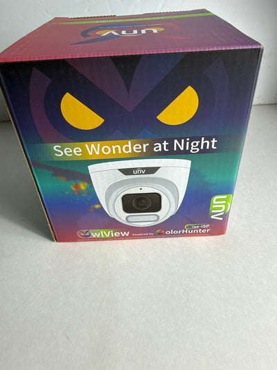 A boxed security camera product on a light gray surface. The box is mostly dark with a colorful gradient, yellow eye graphics, and a printed image of a white dome camera.
