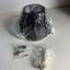 A black cylindrical appliance part, likely a pump or filter component, wrapped in clear plastic packaging, with two small accessory bags containing white fittings and metal pieces on a white surface.