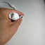 A hand holding a white plastic multi-pin connector next to a small round black-and-white component on a plain light gray surface.