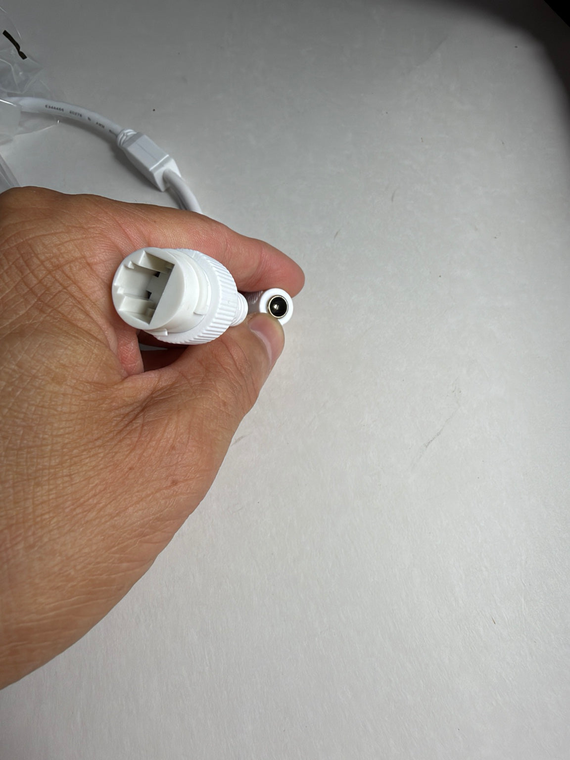 A hand holding a white plastic multi-pin connector next to a small round black-and-white component on a plain light gray surface.