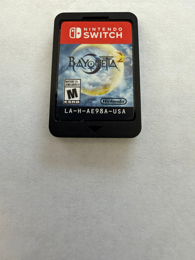 Nintendo Switch Bayoneta 2 game cartridge in a black plastic case with the game cover art visible, placed on a light gray textured surface.