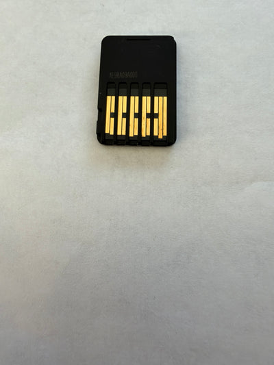 A small black rectangular electronic device with five gold metal contacts on the front, placed on a light gray textured surface.